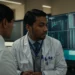 a physician discusses patient care with a colleague in front of a computer screen displaying medical software.