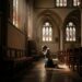 Person in prayer in a church, reflecting on religious vocation discernment